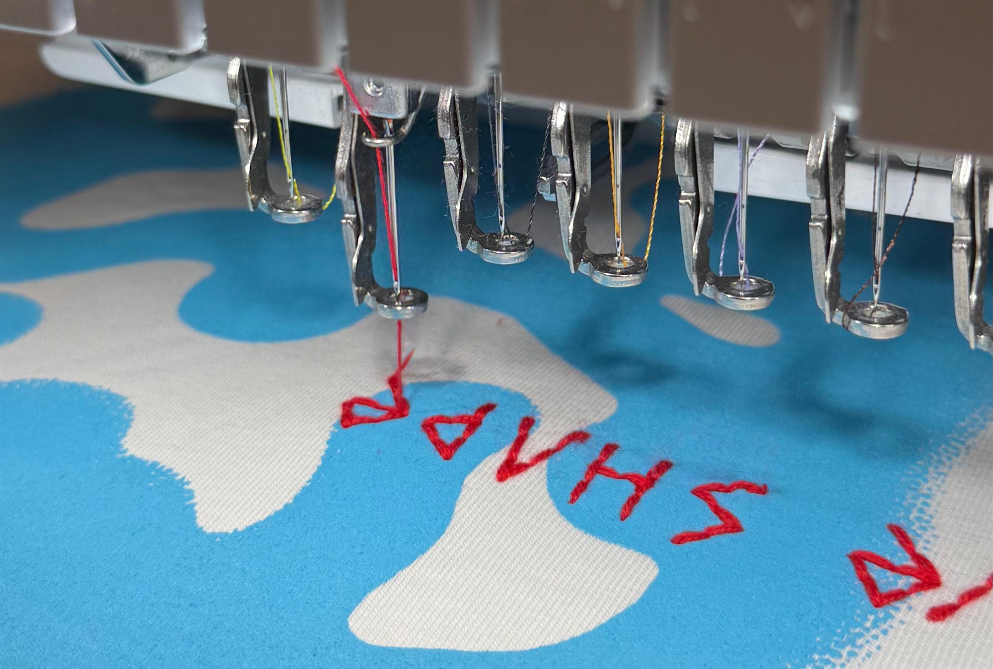Stickmaschine bei der Arbeit, roter Faden auf blauem Stoff